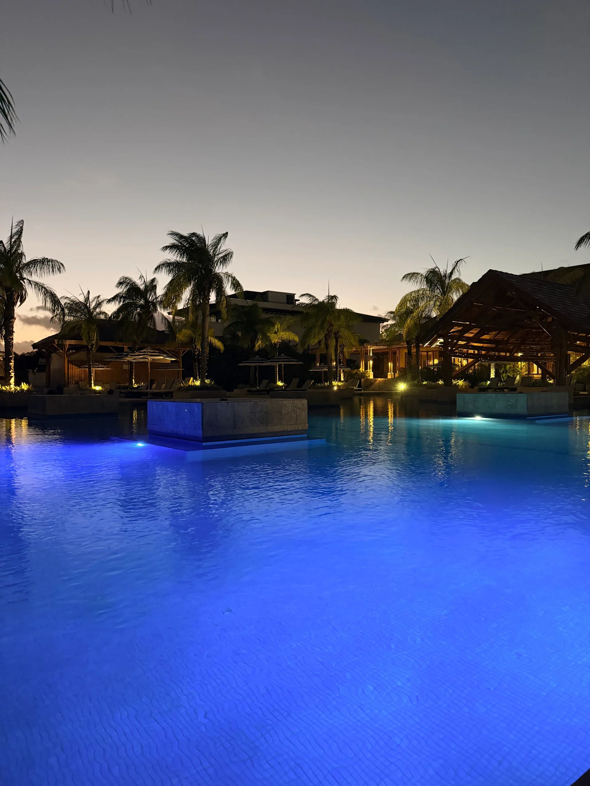 Luxury blue-lit swimming pool at a tropical resort at dusk